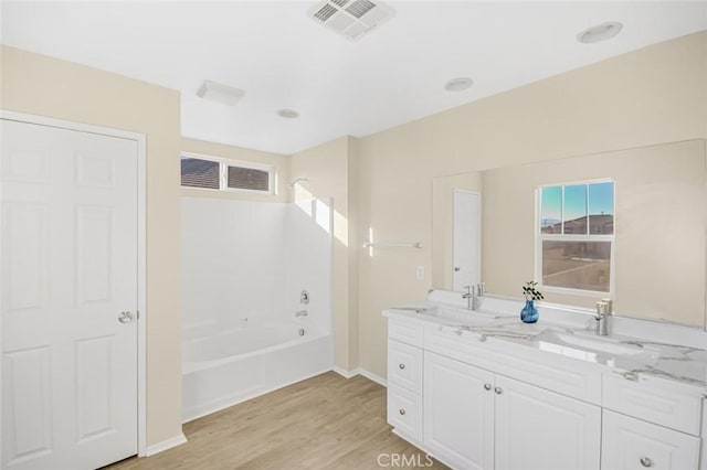 full bath featuring double vanity, wood finished floors, visible vents, a sink, and baseboards