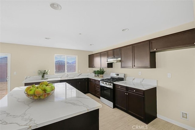 kitchen with light stone counters, under cabinet range hood, light wood finished floors, and stainless steel gas stove