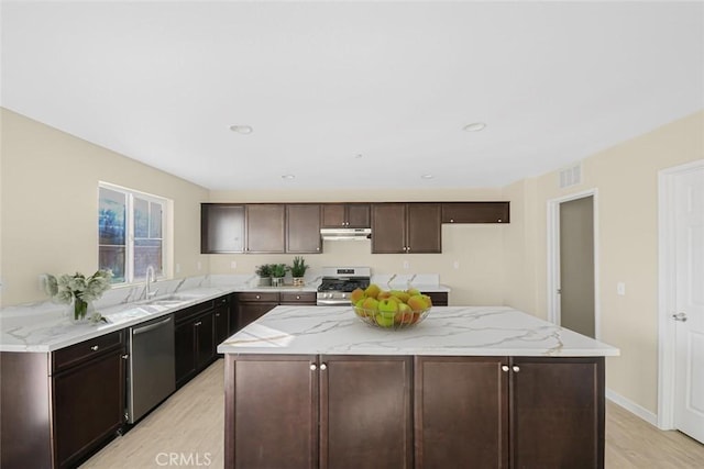 kitchen featuring light wood finished floors, under cabinet range hood, stainless steel appliances, a sink, and a kitchen island