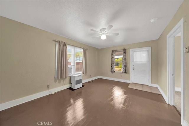unfurnished room featuring dark wood finished floors, baseboards, a ceiling fan, and plenty of natural light