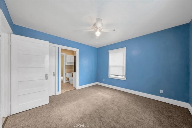 unfurnished bedroom with baseboards, ensuite bathroom, ceiling fan, and carpet