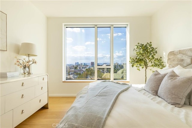 bedroom featuring baseboards, light wood-type flooring, and a city view