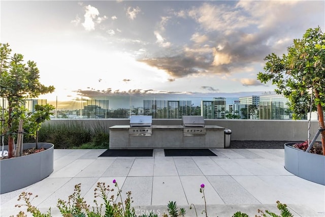 patio terrace at dusk featuring area for grilling, a city view, and exterior kitchen