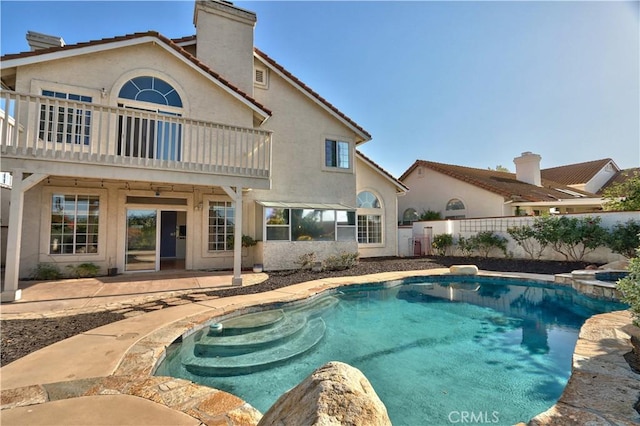 rear view of house with a chimney, a balcony, stucco siding, a patio area, and a pool with connected hot tub