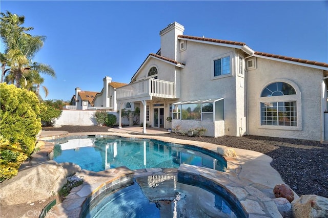 rear view of property with a balcony, a chimney, stucco siding, a patio, and a pool with connected hot tub
