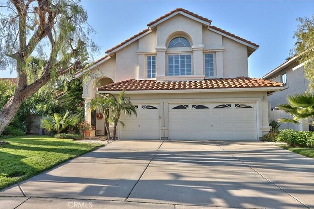 mediterranean / spanish-style house featuring driveway, a tiled roof, a garage, stucco siding, and a front lawn