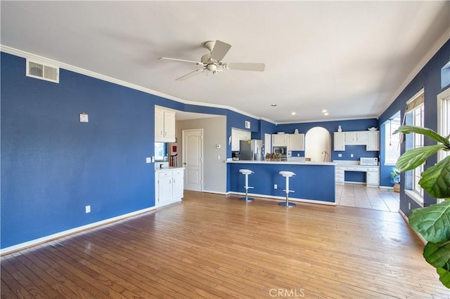 unfurnished living room featuring ceiling fan, light wood finished floors, ornamental molding, baseboards, and arched walkways