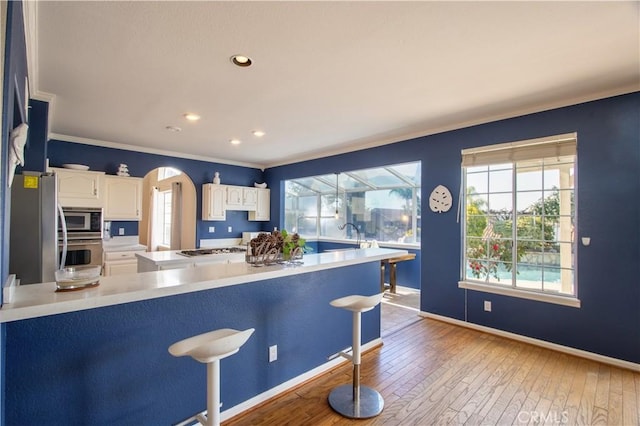 kitchen featuring appliances with stainless steel finishes, wood-type flooring, a breakfast bar area, crown molding, and white cabinets