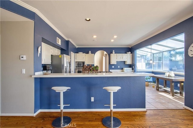 kitchen with appliances with stainless steel finishes, crown molding, white cabinetry, a peninsula, and light wood-type flooring
