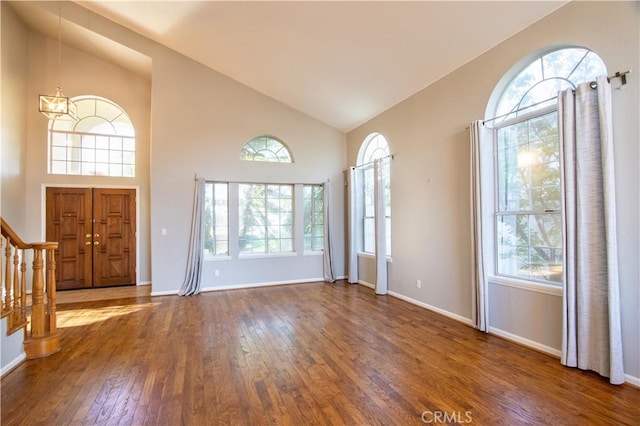 entrance foyer with hardwood / wood-style floors, healthy amount of natural light, stairway, high vaulted ceiling, and baseboards