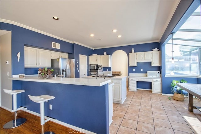 kitchen with appliances with stainless steel finishes, a peninsula, crown molding, white cabinets, and light countertops
