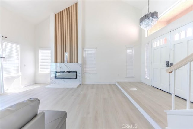 foyer entrance with a high end fireplace, wood finished floors, baseboards, an inviting chandelier, and a high ceiling