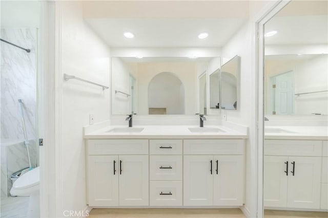 full bath featuring a sink, a marble finish shower, and double vanity