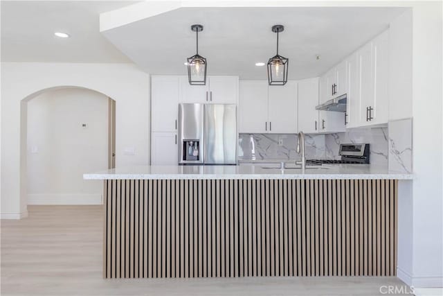 kitchen with appliances with stainless steel finishes, a sink, baseboards, a peninsula, and under cabinet range hood