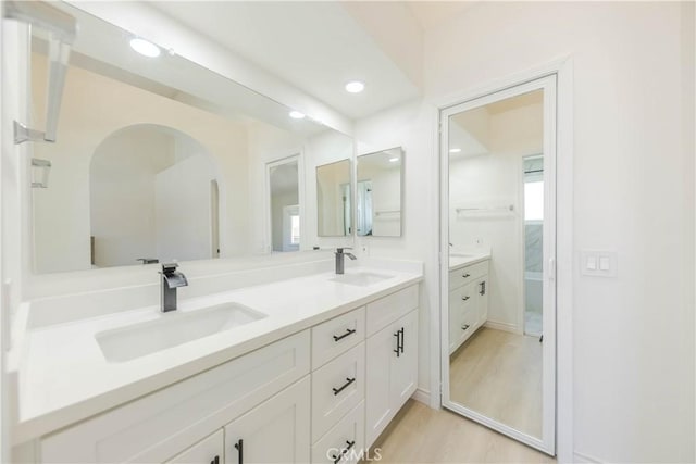 full bath featuring double vanity, recessed lighting, a sink, and wood finished floors