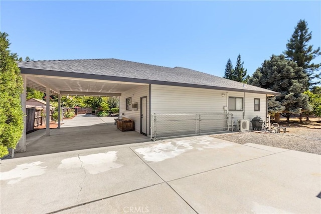 exterior space with ac unit, an attached carport, fence, and a shingled roof