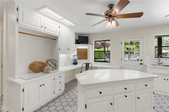 kitchen featuring a ceiling fan, a center island, a sink, light countertops, and white cabinetry