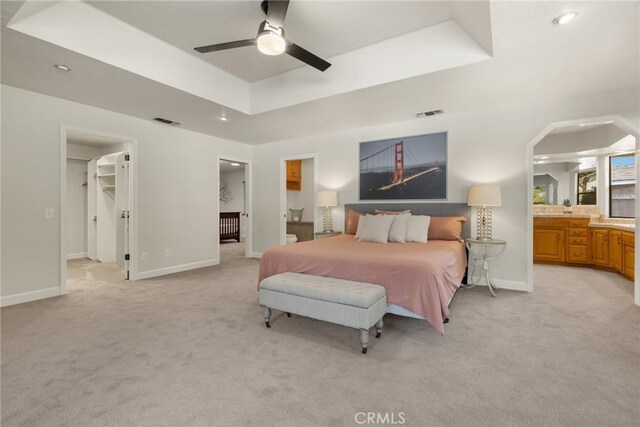 bedroom featuring a raised ceiling, visible vents, light carpet, a walk in closet, and ensuite bathroom
