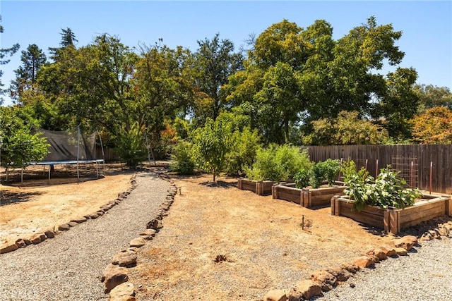view of yard featuring a garden, fence, and a trampoline