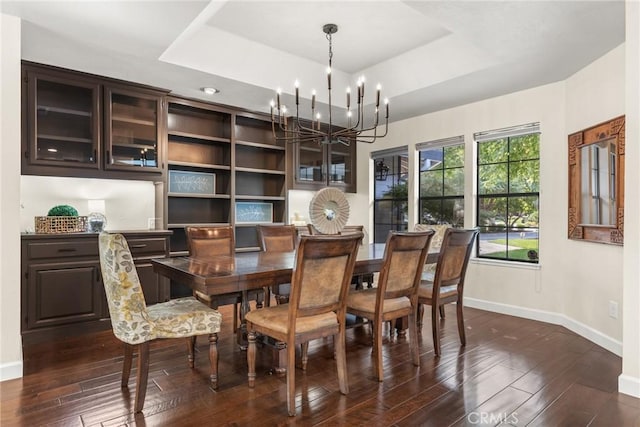 dining area featuring dark wood-type flooring, baseboards, a notable chandelier, and a raised ceiling