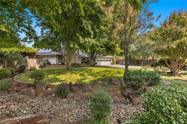 view of front of house featuring an attached garage, concrete driveway, a front lawn, and fence