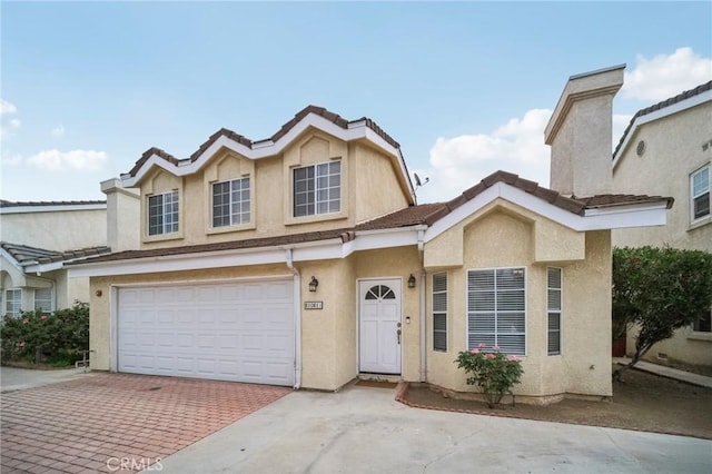 traditional-style home featuring stucco siding, a tile roof, a garage, and decorative driveway