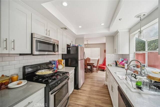 21021 Gault St Unit 9, Canoga Park, CA 91303 - kitchen featuring stainless steel appliances, a tray ceiling, decorative backsplash, light wood-style flooring, and white cabinetry