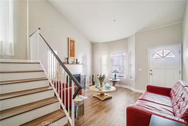 living room featuring stairway, vaulted ceiling, wood finished floors, baseboards, and a fireplace