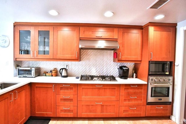 kitchen featuring backsplash, visible vents, appliances with stainless steel finishes, range hood, and light countertops