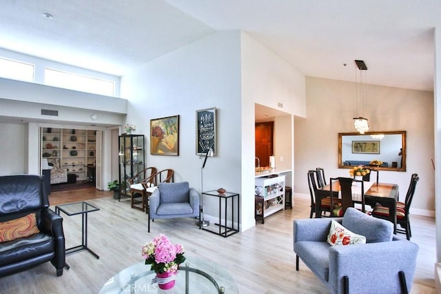 living area with visible vents, baseboards, high vaulted ceiling, and light wood-type flooring
