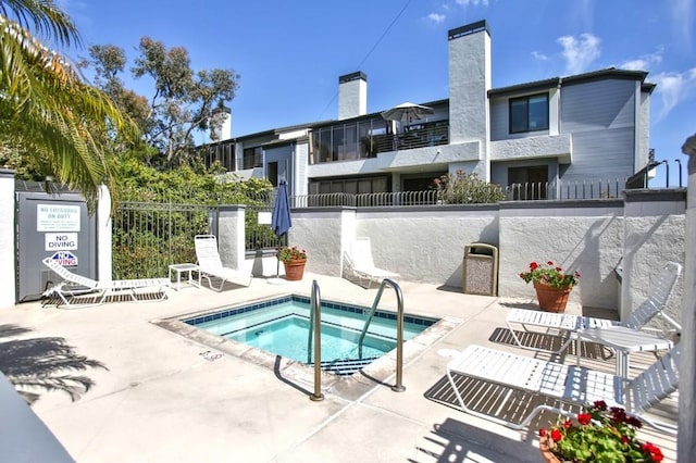 view of swimming pool with a patio, a community hot tub, and fence