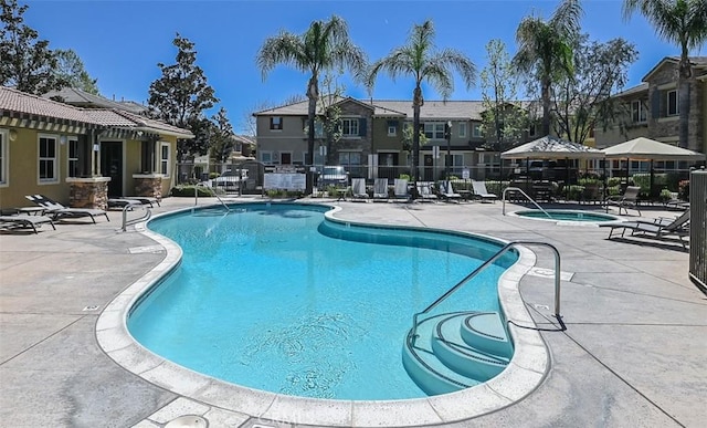 community pool featuring fence, a hot tub, a patio area, and a residential view