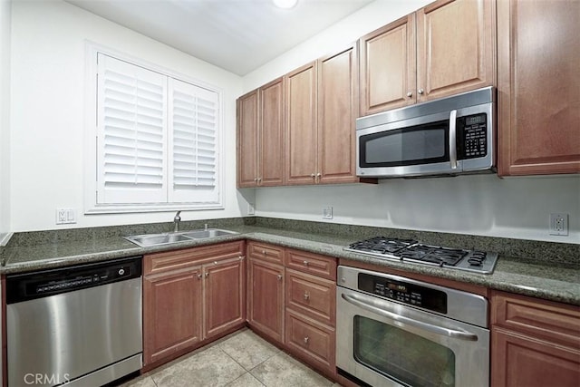 kitchen with light tile patterned floors, dark countertops, stainless steel appliances, and a sink