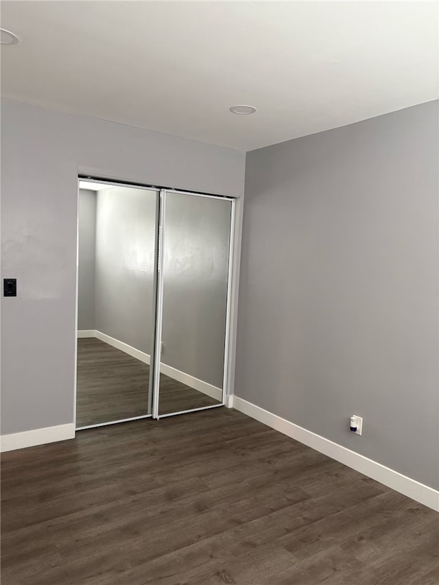 unfurnished bedroom featuring baseboards, dark wood-style flooring, and a closet