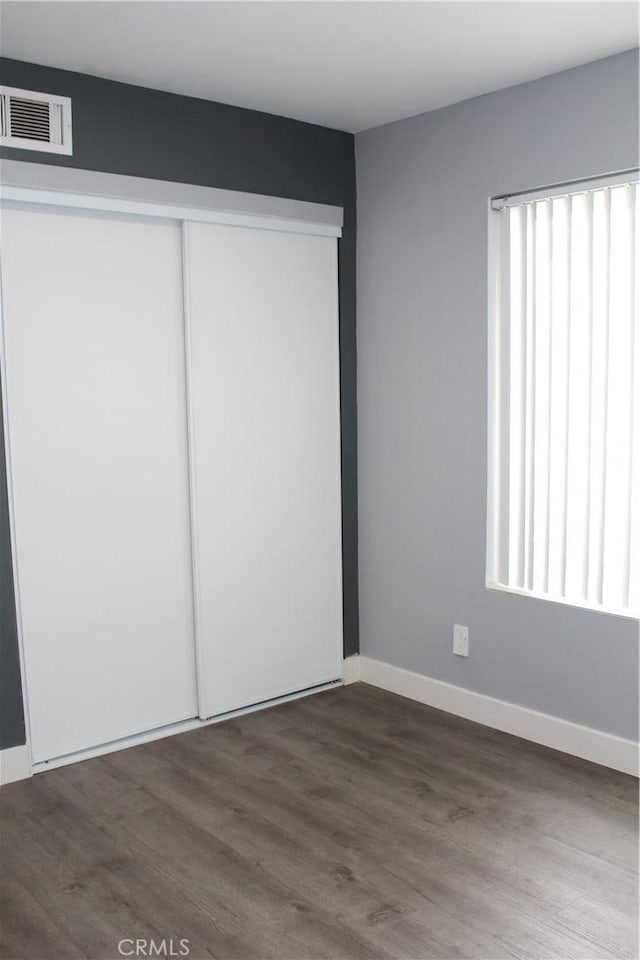 unfurnished bedroom featuring visible vents, baseboards, dark wood finished floors, and a closet