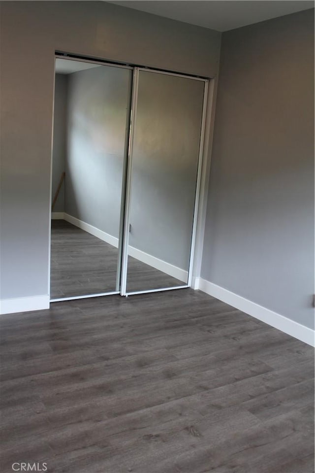 unfurnished bedroom featuring baseboards, wood finished floors, and a closet