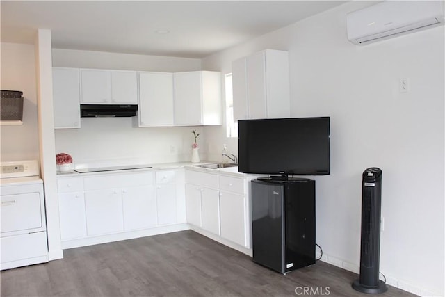 kitchen with dark wood-style flooring, under cabinet range hood, a wall mounted air conditioner, black electric cooktop, and washer / dryer