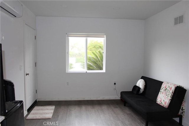 sitting room featuring visible vents, a wall unit AC, and wood finished floors