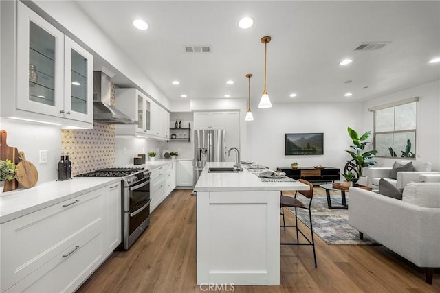 kitchen with a sink, open floor plan, stainless steel appliances, wall chimney exhaust hood, and visible vents