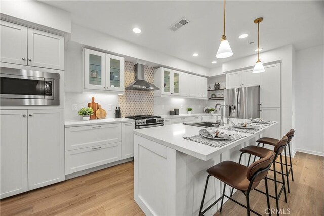 kitchen with recessed lighting, light countertops, a sink, wall chimney exhaust hood, and appliances with stainless steel finishes