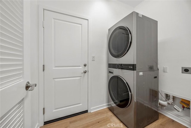 clothes washing area featuring light wood-style flooring, baseboards, stacked washing maching and dryer, and laundry area