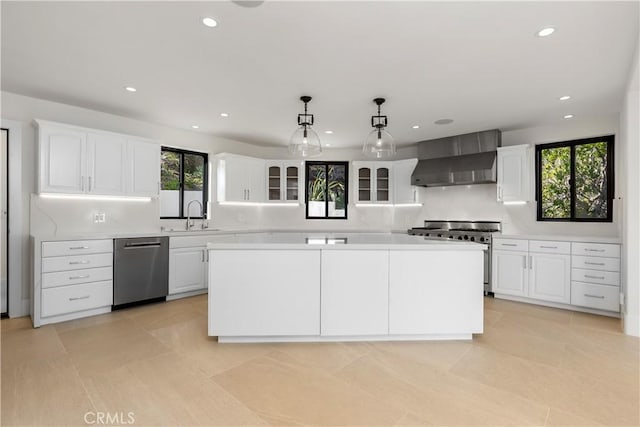 kitchen with appliances with stainless steel finishes, light countertops, wall chimney range hood, a sink, and white cabinetry