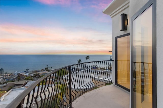 balcony at dusk featuring a water view