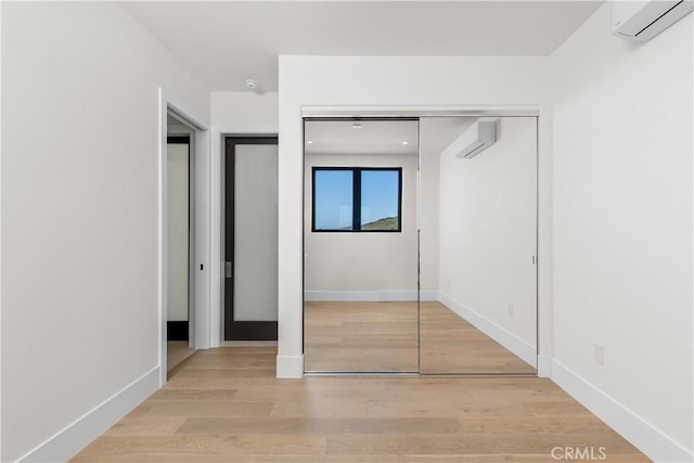 unfurnished bedroom with wood finished floors, a closet, an AC wall unit, and baseboards