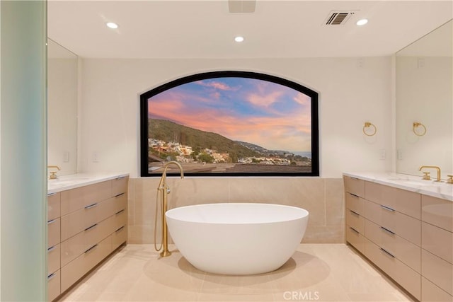 full bathroom featuring tile walls, visible vents, a soaking tub, and vanity