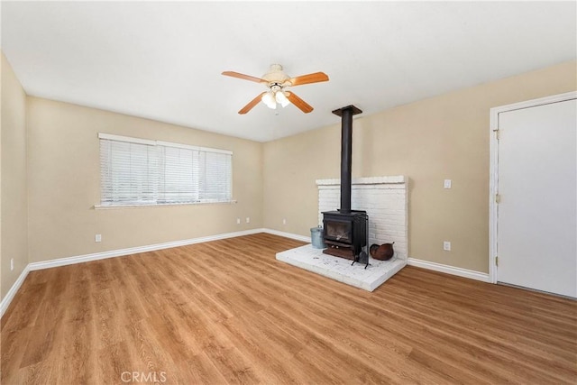 14306 Boxtree St, Lake Hughes, CA 93532 - unfurnished living room with ceiling fan, light wood-style flooring, baseboards, and a wood stove