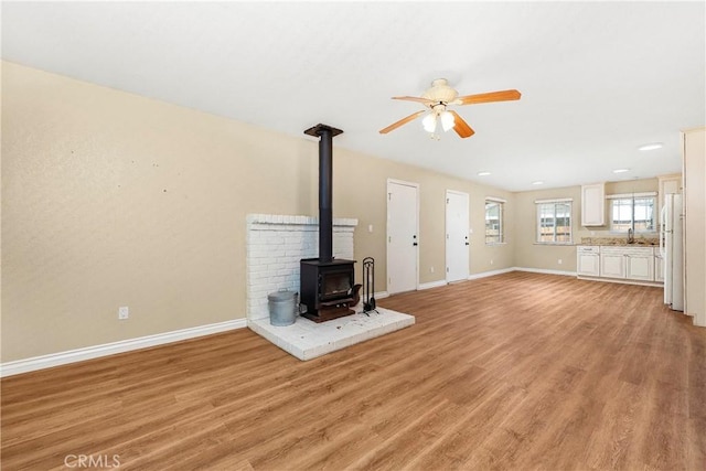 14306 Boxtree St, Lake Hughes, CA 93532 - unfurnished living room featuring a sink, baseboards, light wood-style floors, a ceiling fan, and a wood stove