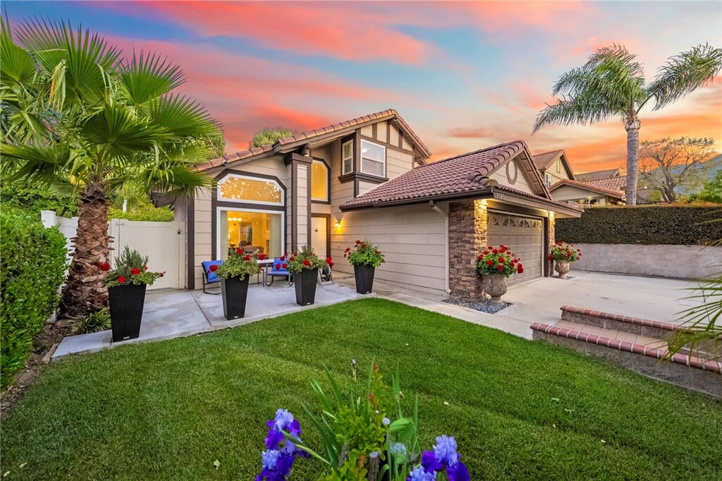 1043 Smoketree Dr, Corona, CA 92882 - back of property at dusk featuring a tile roof, driveway, fence, an attached garage, and a yard