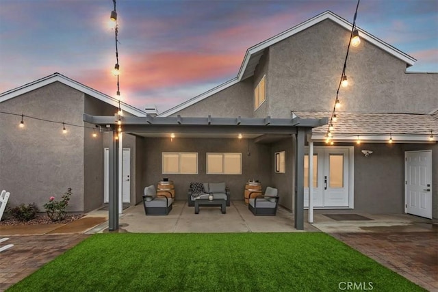 rear view of house with a lawn, a shingled roof, an outdoor hangout area, a patio, and stucco siding
