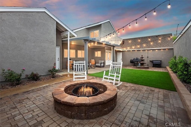 patio terrace at dusk featuring a lawn, a grill, and an outdoor fire pit